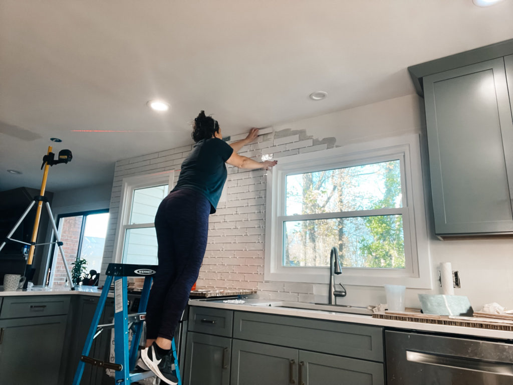 girl installing white tile in an open green kitchen